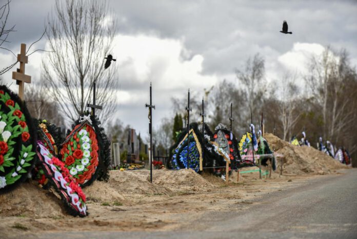 Paukštis skrenda virš naujų kapų Bučos miesto kapinėse, Ukrainoje