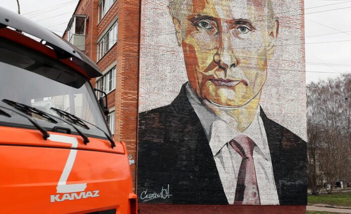 Sunkvežimis su Z raide važiuoja gatve priešais daugiabutį namą su Rusijos prezidento Vladimiro Putino atvaizdu Kaširos mieste, Rusijoje.