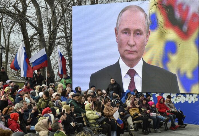 Žmonės po ekranu su Rusijos prezidentu Vladimiru Putinu, dalyvaujantys devintųjų Rusijos įvykdytos Krymo aneksijos metinių renginyje Sevastopolyje (Krymas) / EPA nuotr.