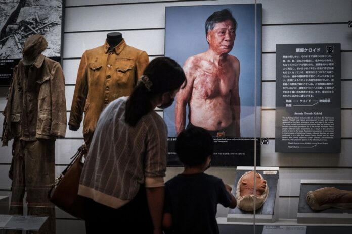 Nagasakio atominės bombos muziejuje Nagasakyje, pietų Japonijoje, berniukas ir jo motina žiūri į atominio bombardavimo aukos Senji Yamaguchi, patyrusio staigius nudegimus, portretą / EPA nuotr.