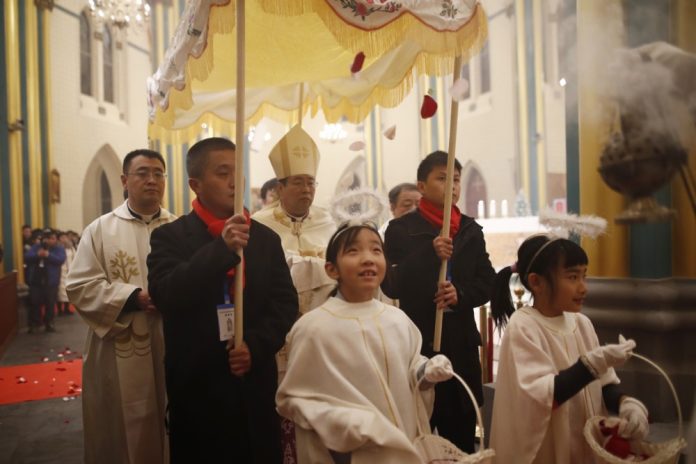 Kinijos vyskupas Josephas Li Shanas (centre) neša Kūdikėlio Kristaus statulėlę Kalėdų išvakarėse Sišiku katalikų bažnyčioje Pekine (Kinija, 2018 m. gruodžio 24 d.) / EPA nuotr.