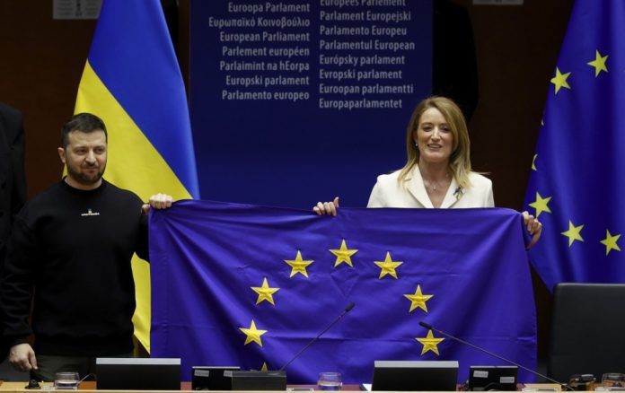 Europos Parlamento pirmininkė Roberta Metsola (R) ir Ukrainos prezidentas Volodymyras Zelenskis (L) laiko ES vėliavą 2023 m. vasario 9 d. Briuselyje (Belgija) vykstančioje specialioje Europos Parlamento sesijoje.